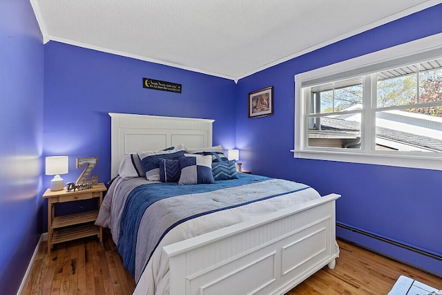 bedroom featuring a baseboard heating unit, wood finished floors, ornamental molding, and baseboards