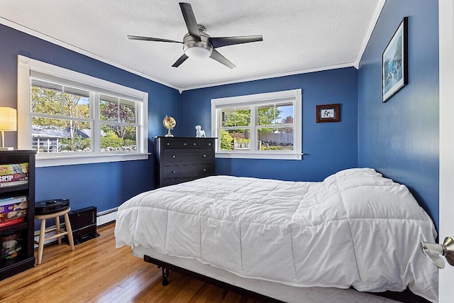 bedroom featuring wood finished floors, a textured ceiling, ceiling fan, crown molding, and baseboard heating