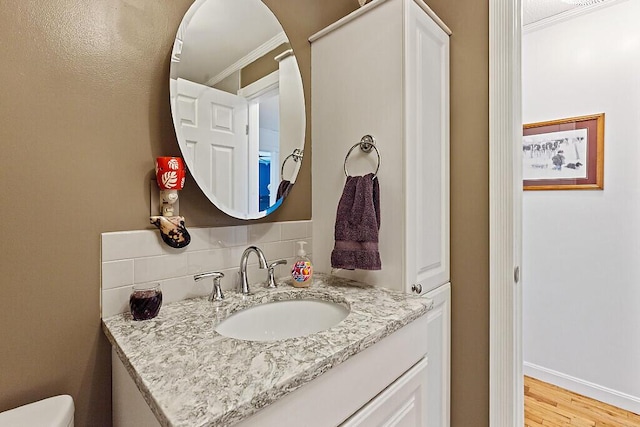 half bath featuring crown molding, decorative backsplash, vanity, wood finished floors, and toilet