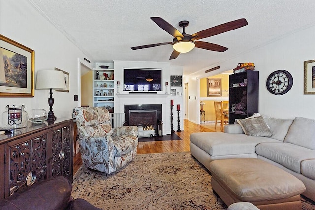 living area featuring wood finished floors, a ceiling fan, a textured ceiling, and a fireplace with flush hearth