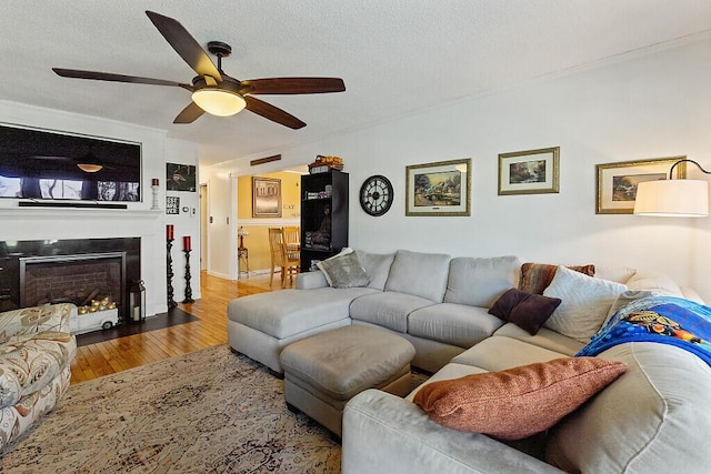 living area featuring wood finished floors, ceiling fan, a fireplace with flush hearth, and a textured ceiling