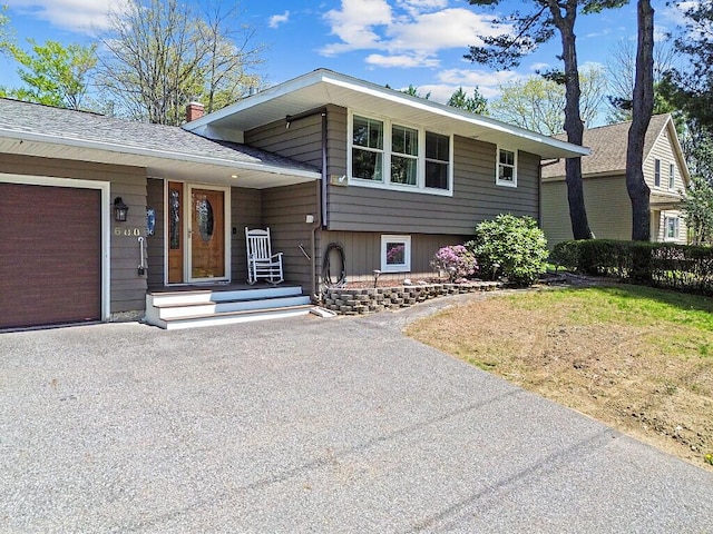 split level home featuring roof with shingles, driveway, an attached garage, and a chimney
