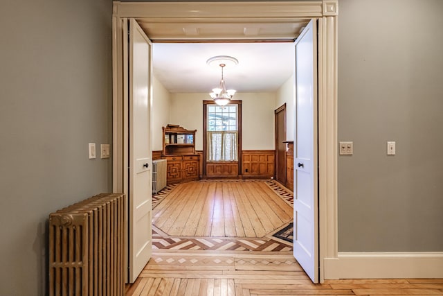 doorway to outside featuring radiator, light wood-style floors, wainscoting, and a chandelier