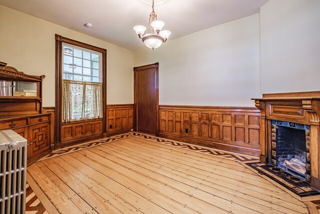 unfurnished dining area with light wood finished floors, wainscoting, a premium fireplace, and a chandelier