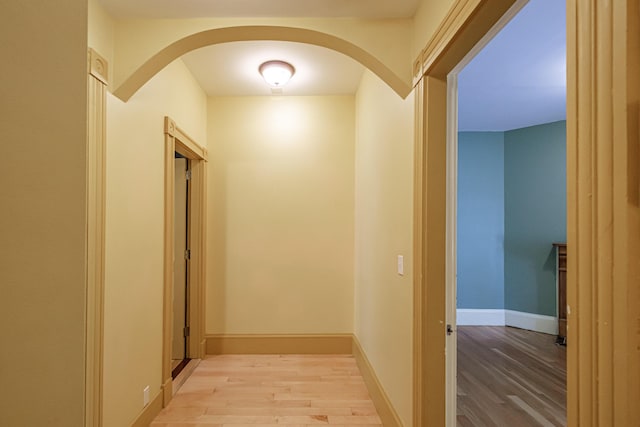 hallway featuring light wood-type flooring, arched walkways, and baseboards