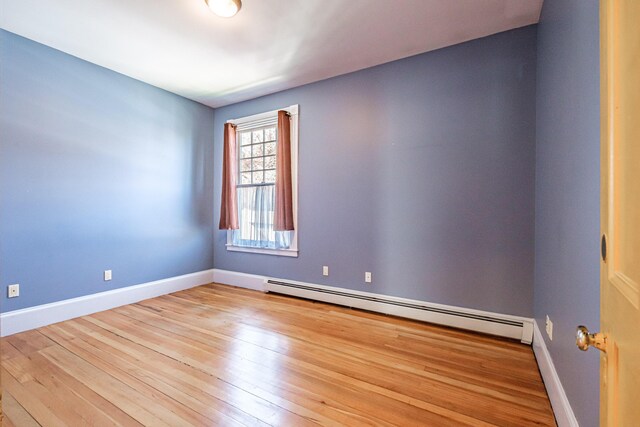 unfurnished room featuring a baseboard heating unit, wood finished floors, and baseboards