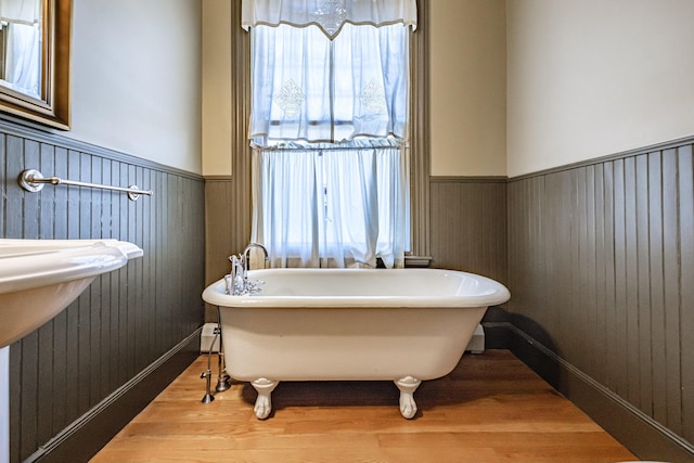 bathroom featuring wood finished floors, a wainscoted wall, a soaking tub, and wood walls