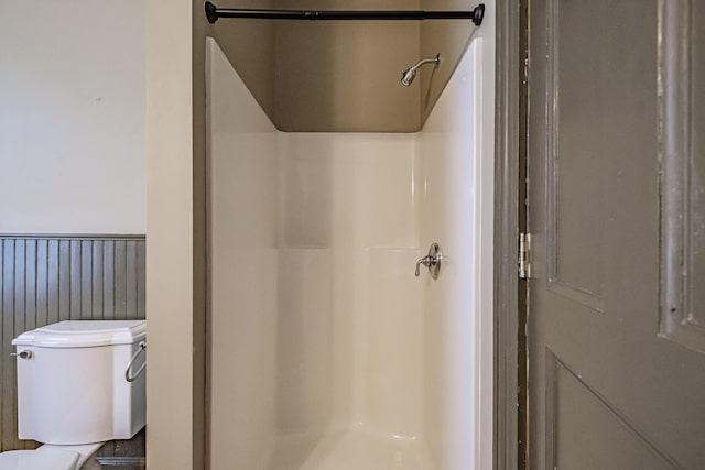 full bath with a shower stall, toilet, and a wainscoted wall