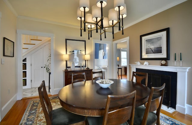131 N St, Bath, ME 04530 - dining room with a chandelier, light wood-style flooring, ornamental molding, baseboards, and a fireplace with raised hearth