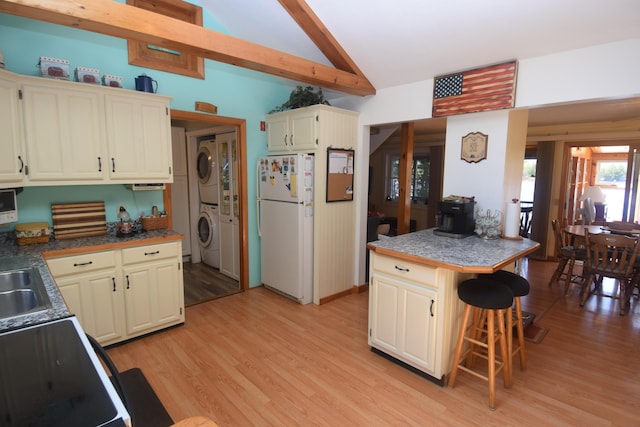 kitchen featuring freestanding refrigerator, stacked washer and clothes dryer, a kitchen bar, light wood-style floors, and a peninsula