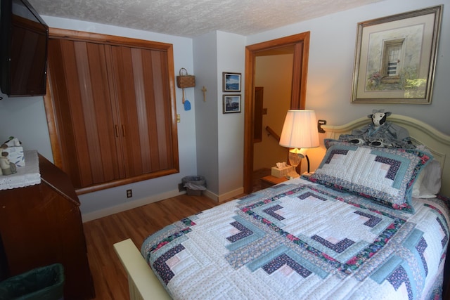bedroom with wood finished floors, baseboards, and a textured ceiling