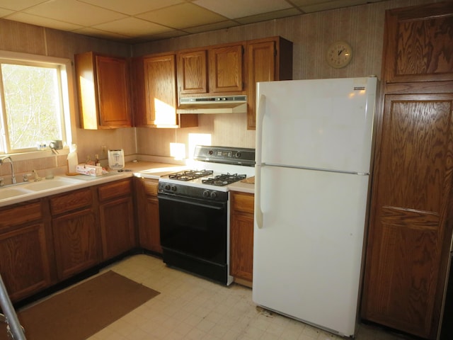 kitchen featuring freestanding refrigerator, range with gas stovetop, under cabinet range hood, light flooring, and brown cabinets