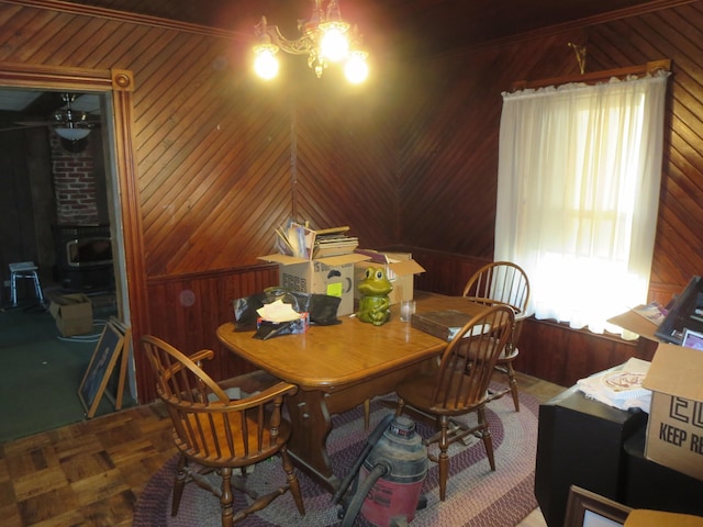 dining space with wood walls, a chandelier, and a wood stove