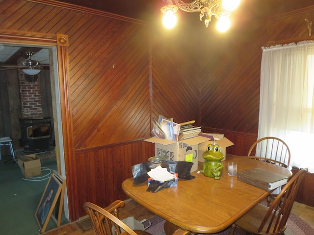 dining space with wood walls, a wood stove, and a chandelier