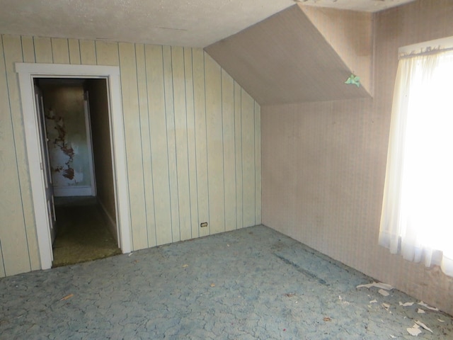 additional living space featuring vaulted ceiling, wood walls, carpet, and plenty of natural light