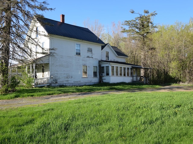 back of property with a chimney, a sunroom, metal roof, and a lawn
