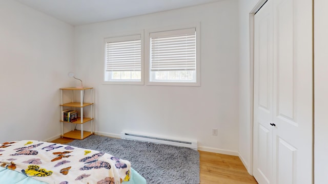 bedroom featuring a baseboard radiator, a closet, light wood-style flooring, and baseboards