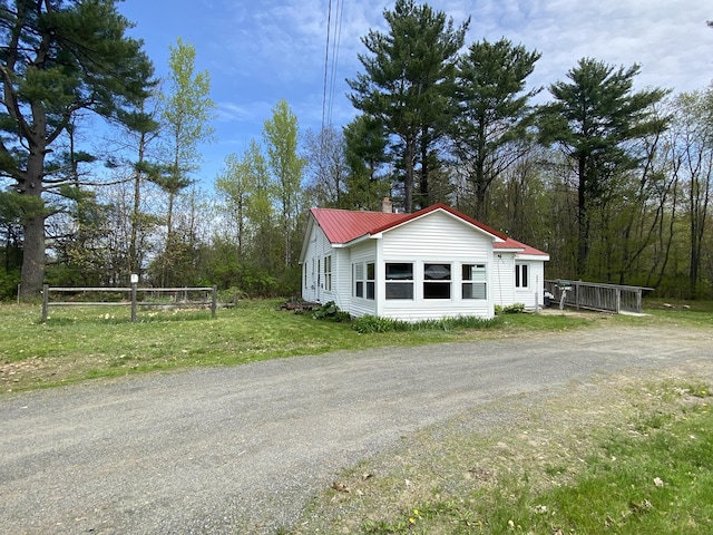 view of side of home with dirt driveway, a yard, and metal roof