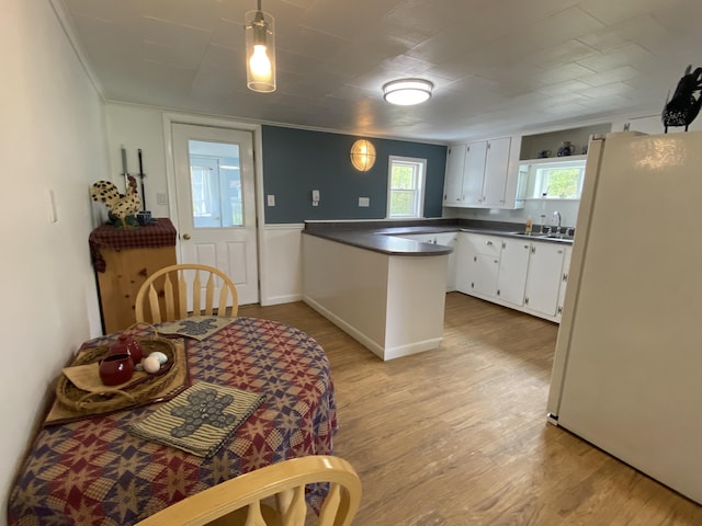 kitchen with freestanding refrigerator, a peninsula, dark countertops, a sink, and light wood-style flooring