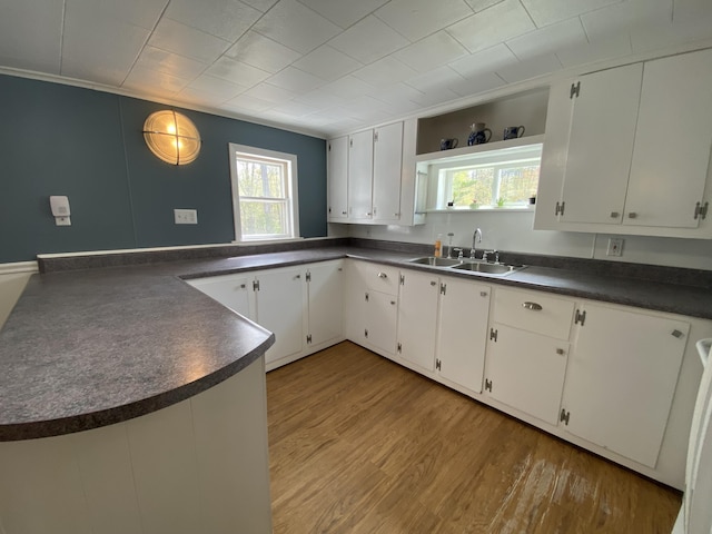 kitchen featuring dark countertops, a sink, light wood-style floors, and white cabinetry