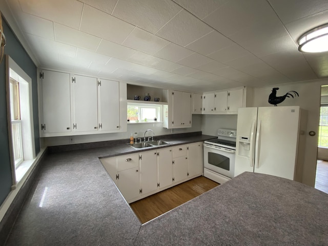 kitchen with white appliances, a sink, dark countertops, wood finished floors, and white cabinetry