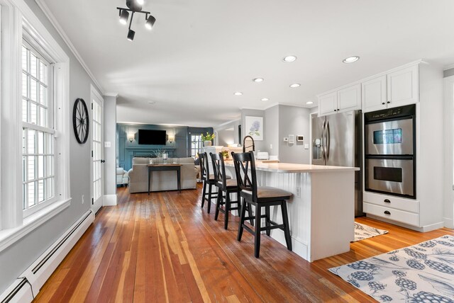70 Summer St, Kennebunk, ME 04043 - kitchen with stainless steel double oven, a baseboard radiator, light wood-style flooring, a breakfast bar, and white cabinetry