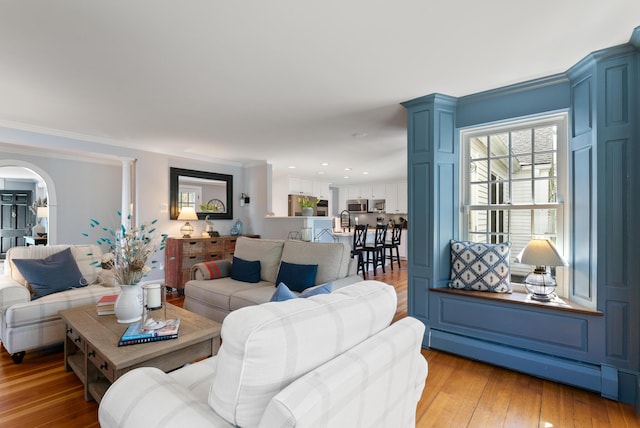 70 Summer St, Kennebunk, ME 04043 - living room with a baseboard radiator, light wood-style floors, arched walkways, and crown molding