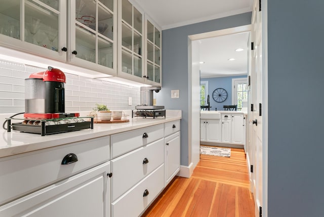 70 Summer St, Kennebunk, ME 04043 - kitchen with light wood-type flooring, backsplash, crown molding, light countertops, and white cabinetry