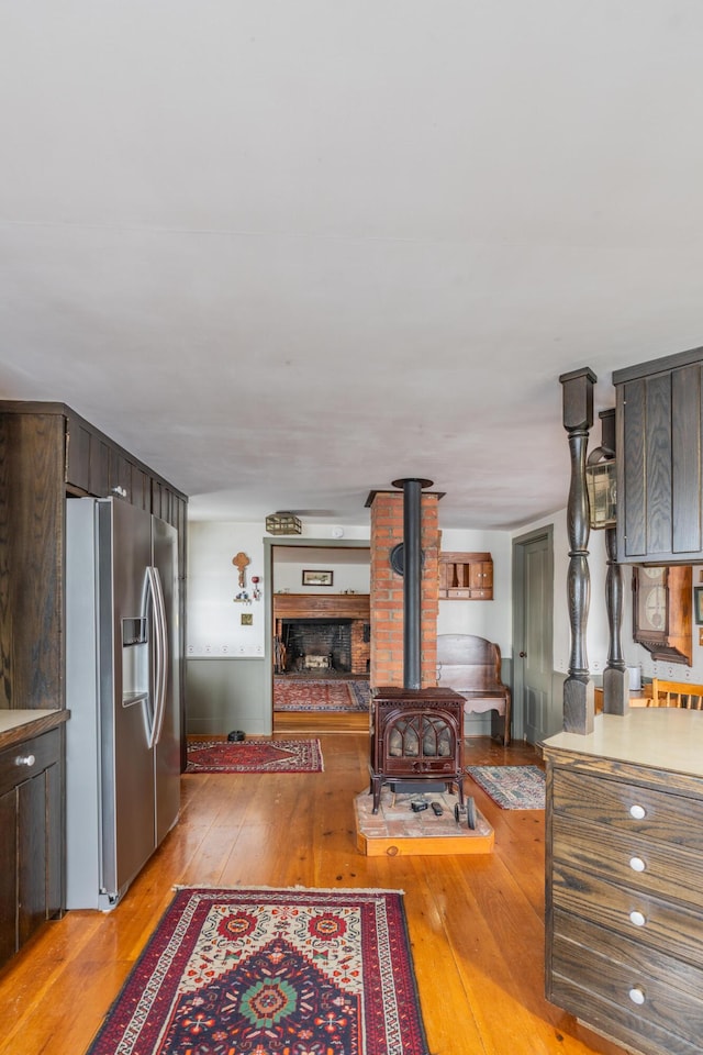 kitchen with stainless steel fridge, light wood-style floors, a wood stove, and dark brown cabinetry