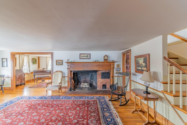 living room with wood finished floors, stairway, and a fireplace with raised hearth