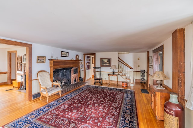 living room featuring light wood-style floors, stairs, a fireplace with raised hearth, and baseboards