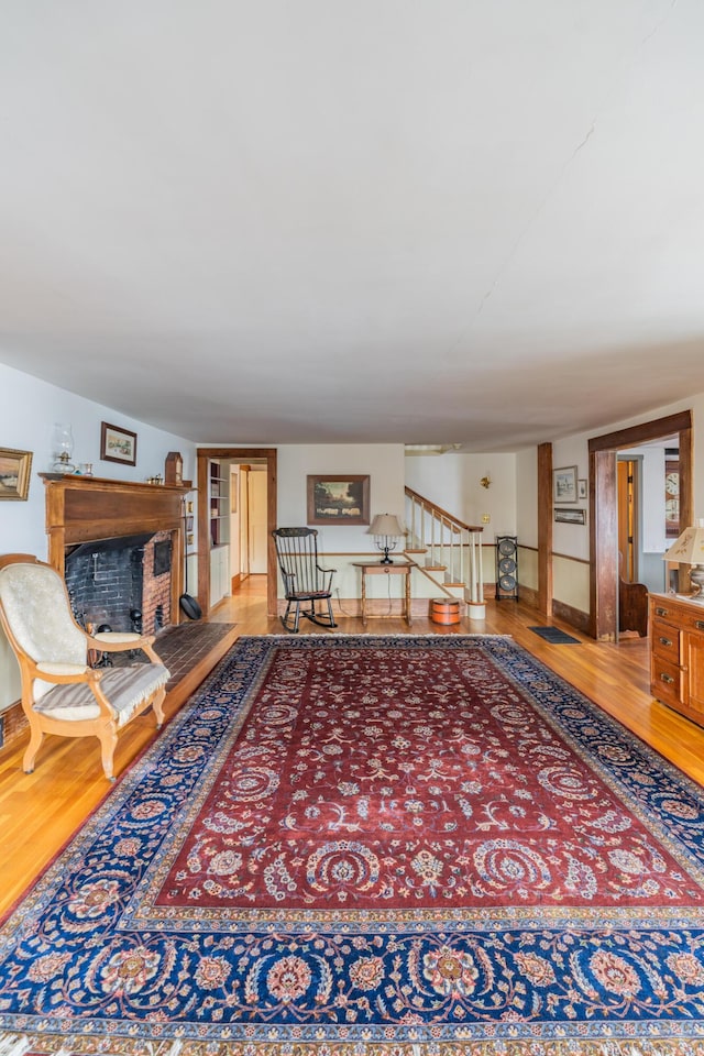 living area with a fireplace with raised hearth, wood finished floors, stairway, and baseboards