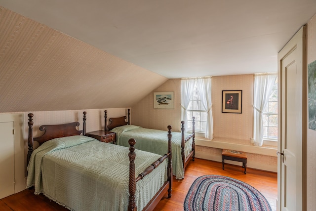 bedroom with wood finished floors, lofted ceiling, and wallpapered walls