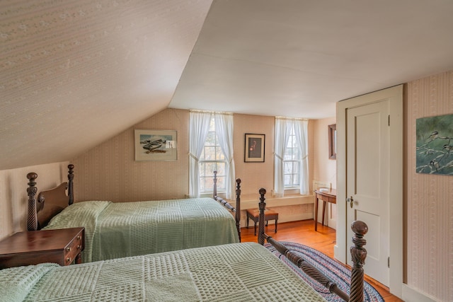 bedroom featuring wallpapered walls, light wood-type flooring, and lofted ceiling