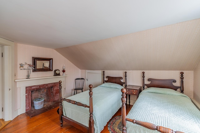 bedroom featuring wood finished floors, lofted ceiling, a fireplace, and wallpapered walls