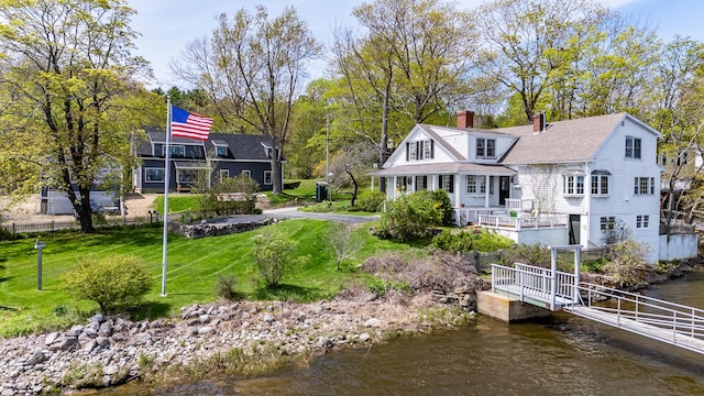 rear view of property with a chimney, a water view, and a yard