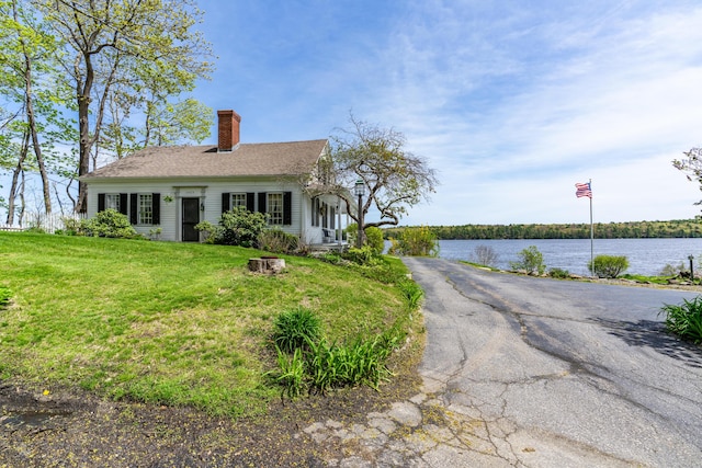 view of front of house featuring a chimney, a front yard, and a water view