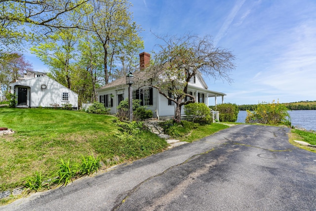 view of front of house featuring a chimney, a front lawn, covered porch, and a water view