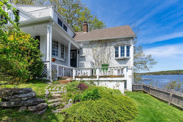 view of front of home with a chimney, a water view, and a shingled roof