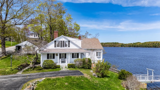 view of front facade with a porch, a chimney, a water view, and a front yard