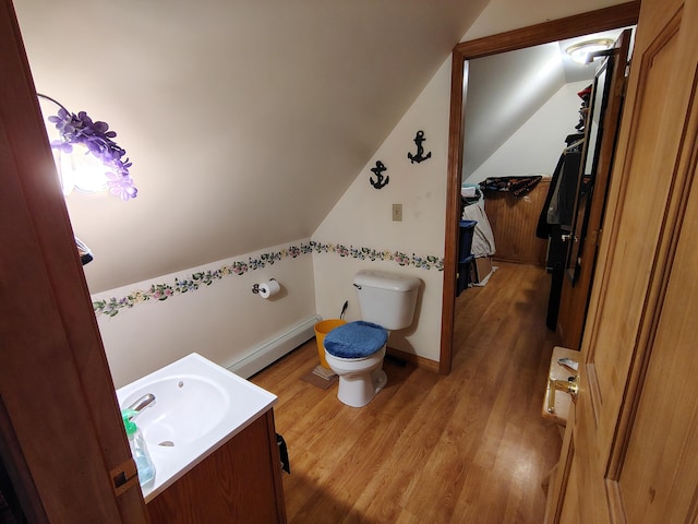 half bath with a baseboard radiator, lofted ceiling, wood finished floors, vanity, and toilet