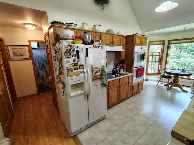 kitchen featuring white appliances, under cabinet range hood, brown cabinetry, vaulted ceiling, and light countertops