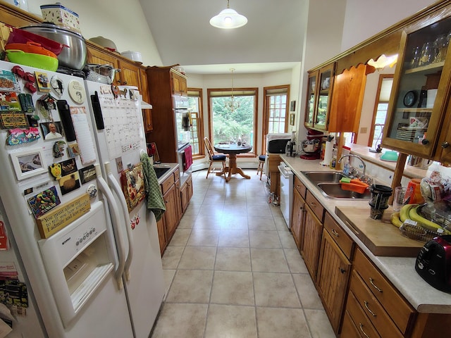 kitchen featuring white appliances, brown cabinetry, a sink, light tile patterned floors, and light countertops