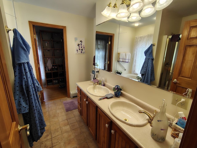 bathroom with a chandelier, double vanity, stone finish flooring, and a baseboard radiator