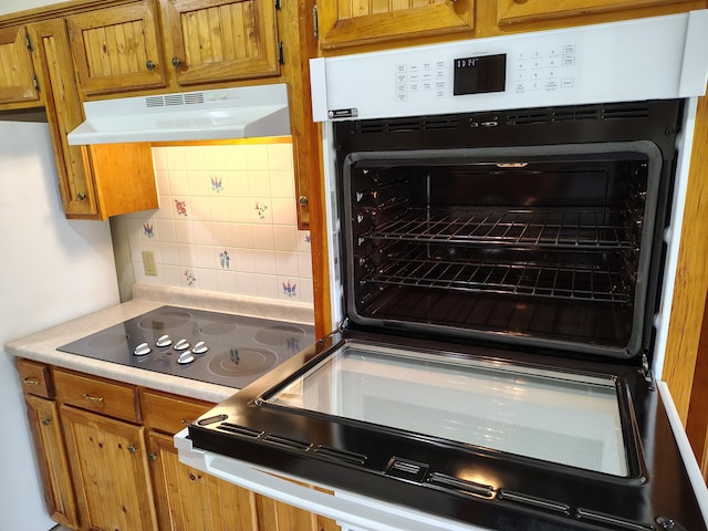 100 Weber Ln, Calais, ME 04619 - kitchen with under cabinet range hood, black electric cooktop, decorative backsplash, brown cabinets, and light countertops