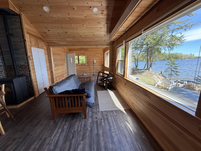 sunroom / solarium featuring a wood stove, vaulted ceiling, and a water view