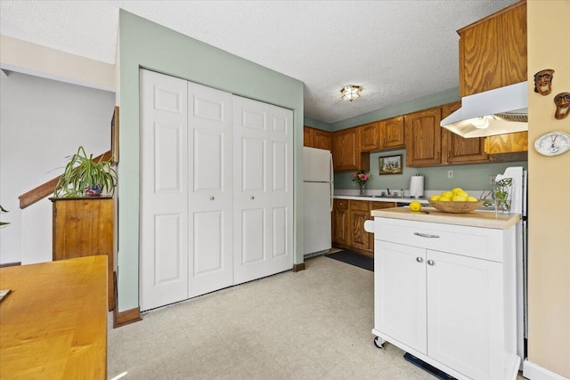 18 Ocean St Unit 72, South Portland, ME 04106 - kitchen with freestanding refrigerator, light countertops, under cabinet range hood, light floors, and brown cabinets