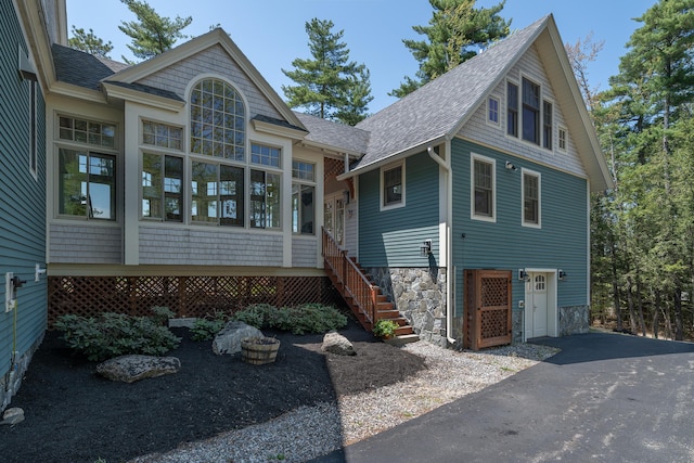 view of front of home featuring roof with shingles, asphalt driveway, and stairway