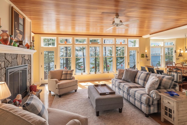 living room with wooden ceiling, a ceiling fan, light wood-type flooring, and a stone fireplace