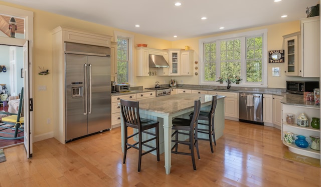 kitchen with stainless steel appliances, under cabinet range hood, healthy amount of natural light, a kitchen breakfast bar, and recessed lighting
